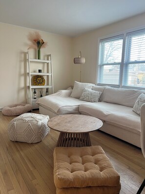 A cozy living room with a sectional sofa, a round coffee table, and a tufted ottoman. - Cozy 2-bedroom condo with AC in gorgeous Chicago neighborhood (Chicago)