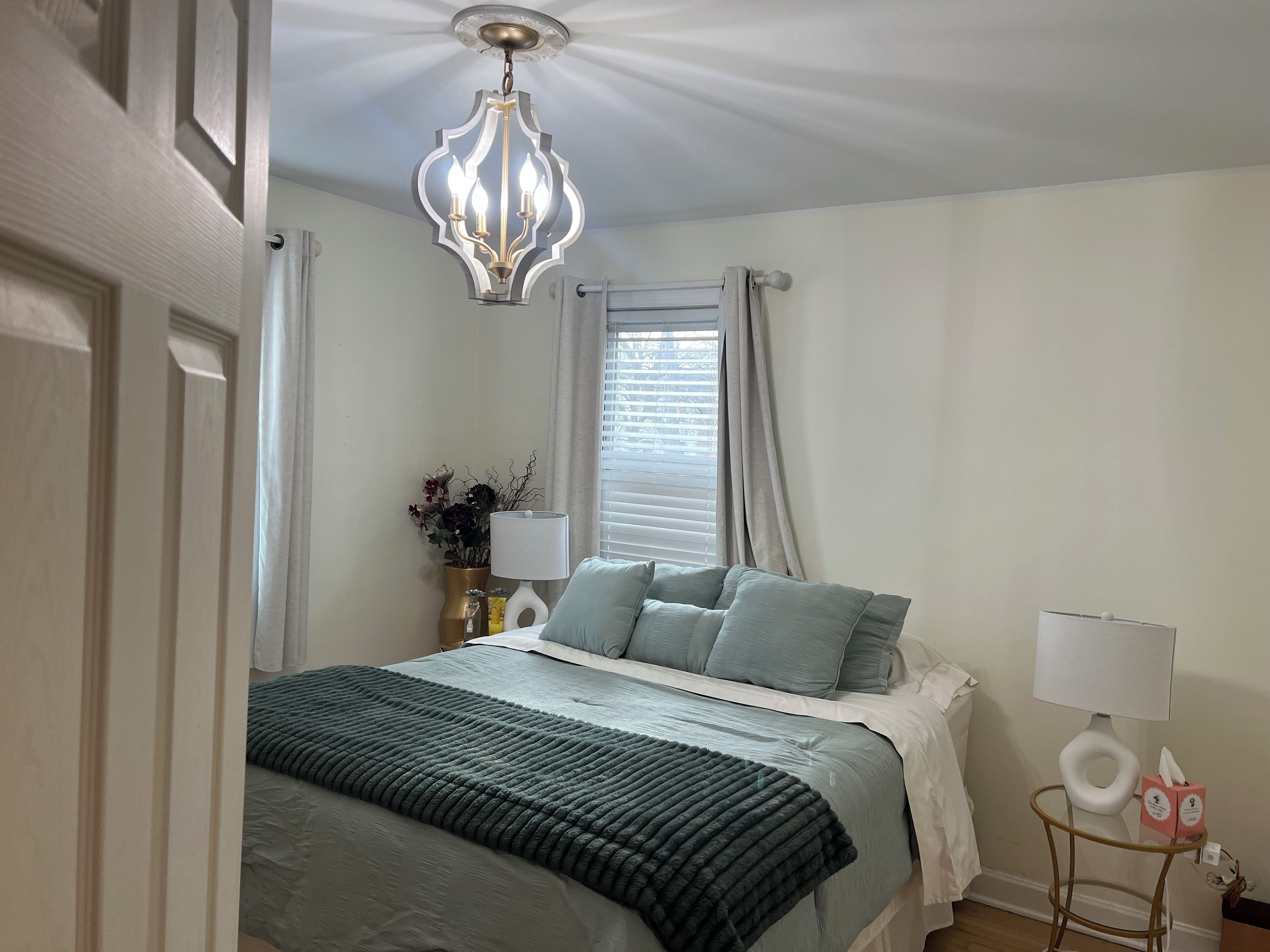A bedroom with a bed, a bedside table, a lamp, and a window with curtains.