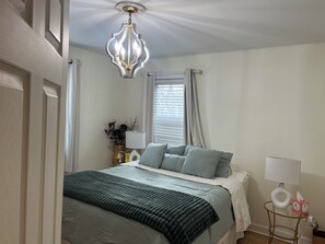 Quarto com cama, mesa de cabeceira, abajur e janela com cortinas.