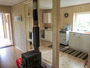 Interior de una cabaña con paredes de madera, una zona de cocina con estufa y armarios, y un estuche rojo para herramientas.