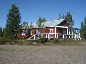 A red wooden house with a porch and a metal roof, surrounded by trees.