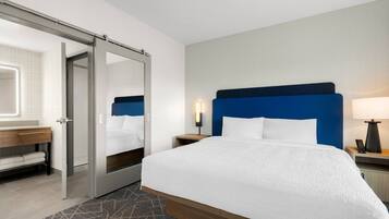 A hotel room with a bed, a bathroom with a mirror, and a nightstand with a lamp.