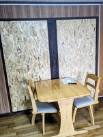 Una mesa de madera con dos sillas, un objeto negro sobre la mesa y una pared con un panel vertical negro.