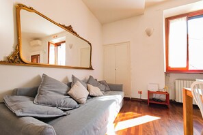Una habitación con un sofá gris, un espejo grande, una puerta blanca y una ventana con vistas.