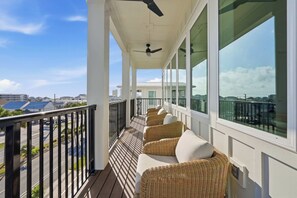 Ein überdachter Balkon mit Korbmöbeln, großen Fenstern und einem Deckenventilator.