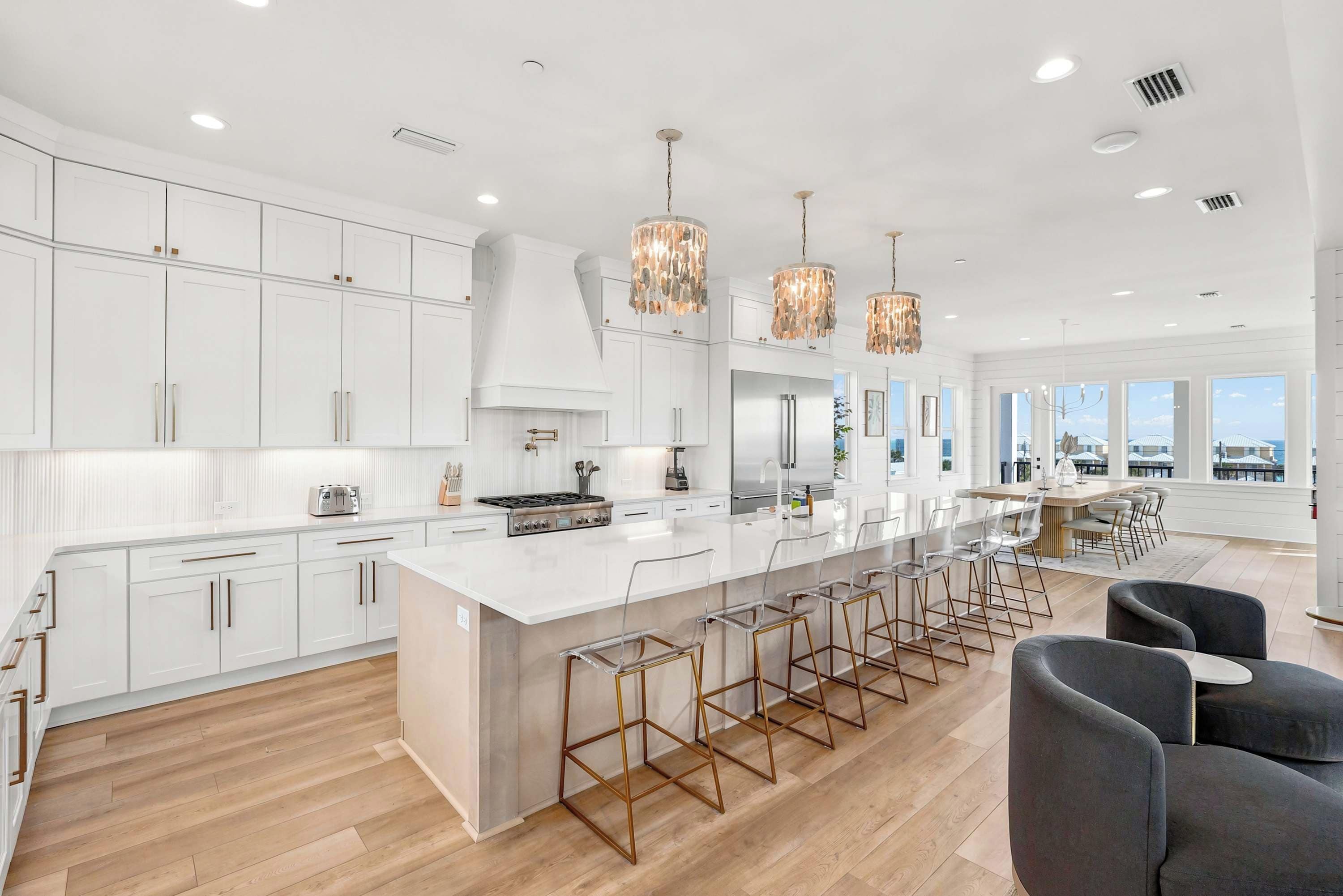 A modern kitchen with white cabinetry, a central island, bar stools, and pendant lighting.