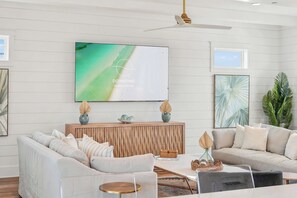 Un salon moderne avec un canapé, une table basse et un téléviseur diffusant des publicités pour « DOWNTIME Vacation Rentals ».