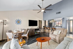 A modern living room with a dining area, a kitchen, and a ceiling fan. - Inverness on the Green | Golf Course Views | Modern 2BR | Pool & Tennis | Palm Desert (Palm Desert)