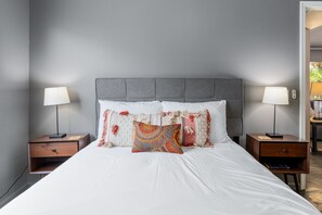 A neatly made bed with white linens and decorative pillows, flanked by two bedside tables with lamps, against a plain wall. - Inverness on the Green | Golf Course Views | Modern 2BR | Pool & Tennis | Palm Desert (Palm Desert)