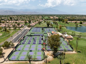 Un gran complejo de tenis con varias canchas, rodeado de edificios residenciales y un lago.