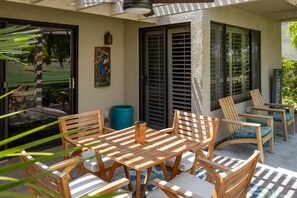 Un patio al aire libre con una mesa y sillas de madera, una maceta azul y un cuadro en la pared.