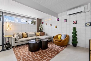 A modern living room with a sectional sofa, a round coffee table, a brown armchair, and a patterned rug. - Mod Pad 2.0 | Historic Ocotillo Lodge | Pool (Palm Springs)