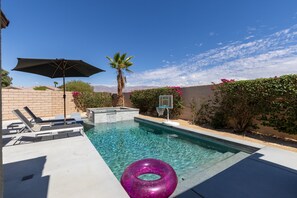 Een zwembad met een jacuzzi, ligbedden en een basketbalring.