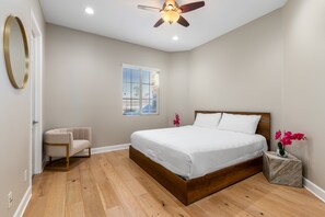 A bedroom with a bed, a chair, a window with blinds, a ceiling fan, and a small plant on a nightstand. - Lago Vista Retreat | Pool & Game Room | Half Court Basketball | 4BR (Indio)