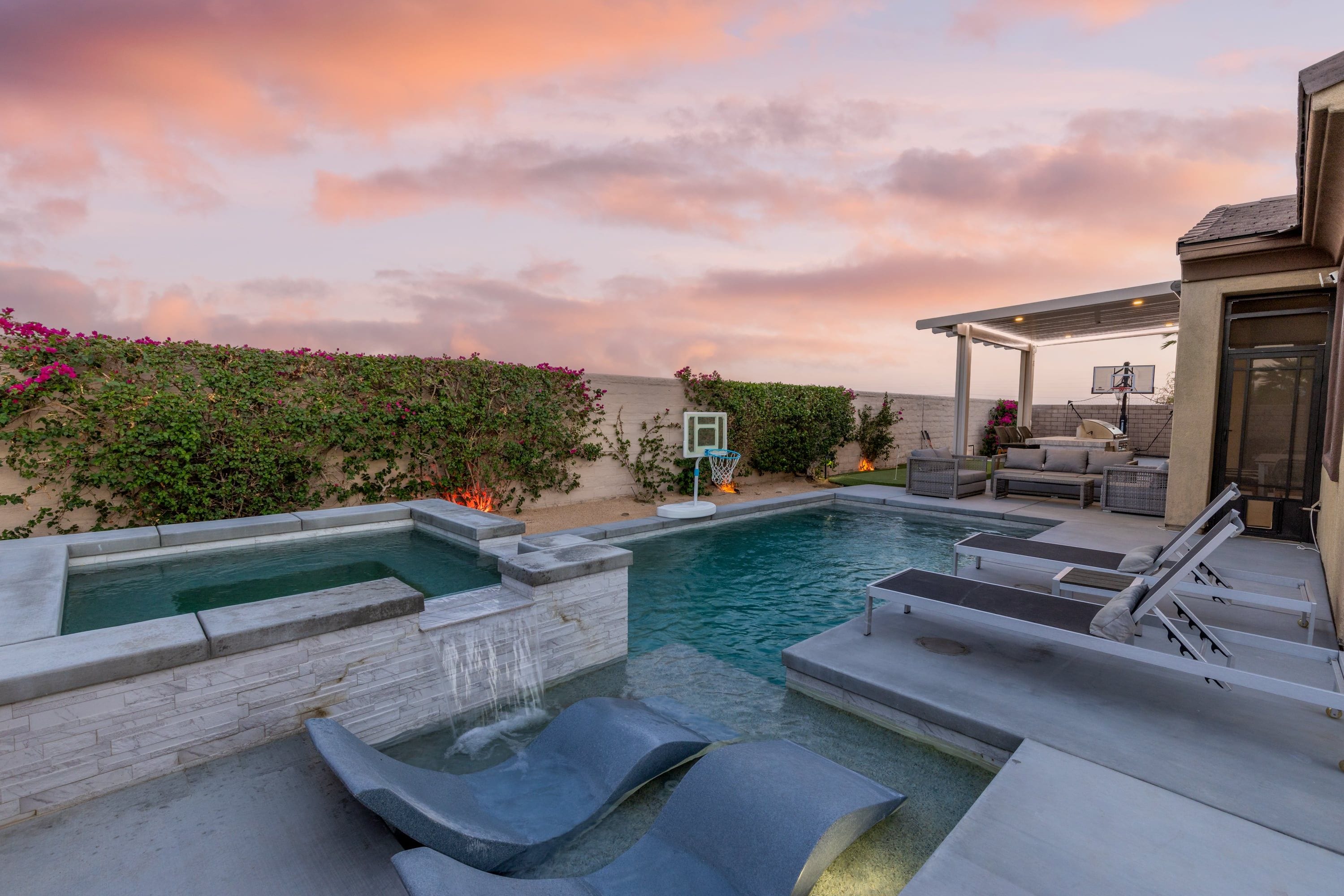 A swimming pool with a waterfall feature, lounge chairs, and a covered seating area.