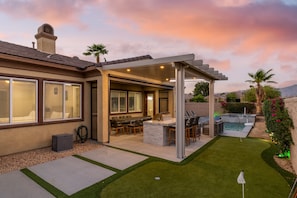 A residential backyard with a covered patio, outdoor seating, a pool, and a well-maintained lawn. - Lago Vista Retreat | Pool & Game Room | Half Court Basketball | 4BR (Indio)