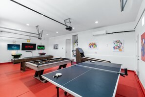 A recreational room with pool tables, a ping pong table, and wall-mounted screens displaying streaming services. - Lago Vista Retreat | Pool & Game Room | Half Court Basketball | 4BR (Indio)