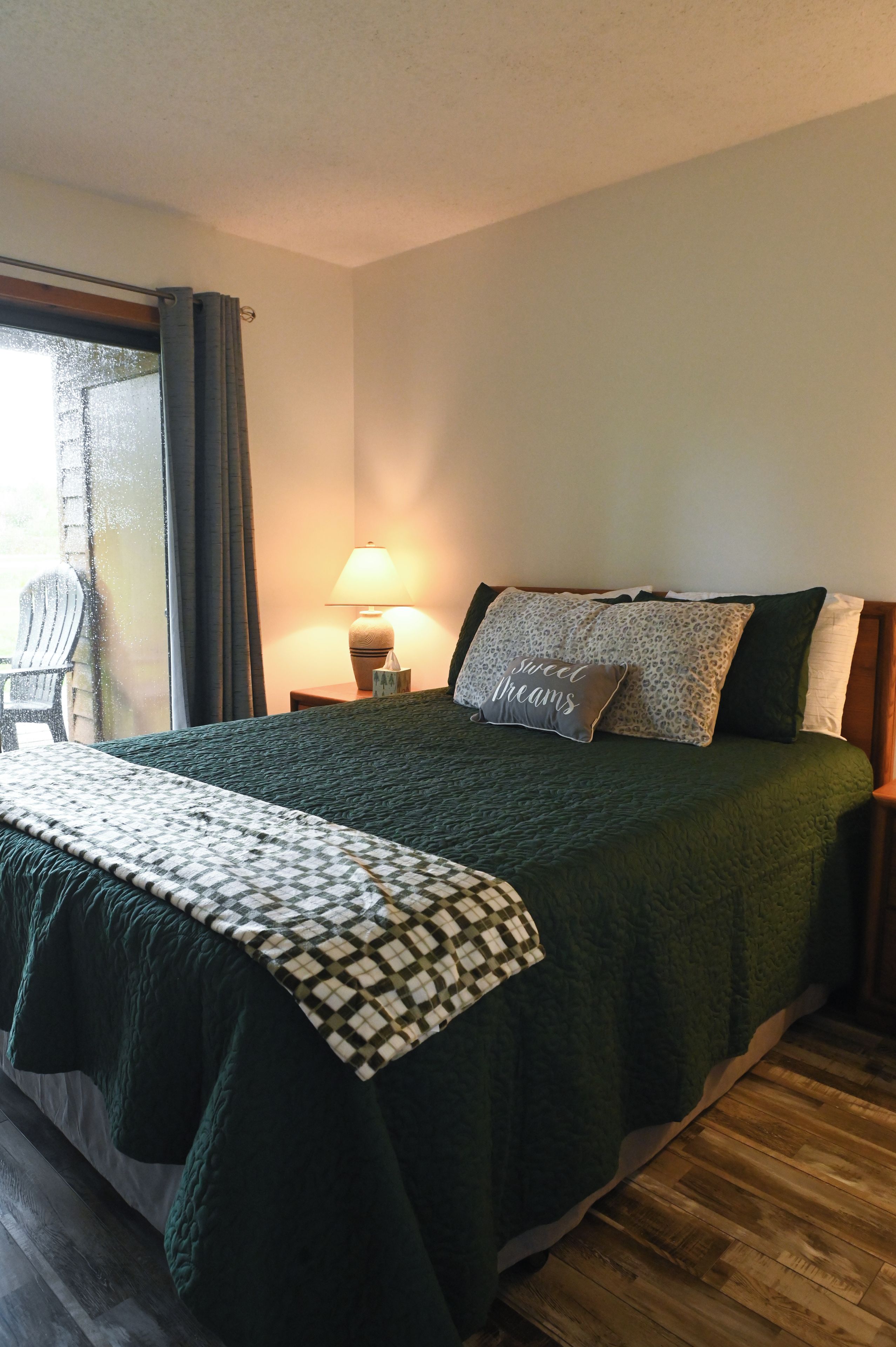 A bedroom with a bed, a nightstand, a lamp, and a window with curtains.