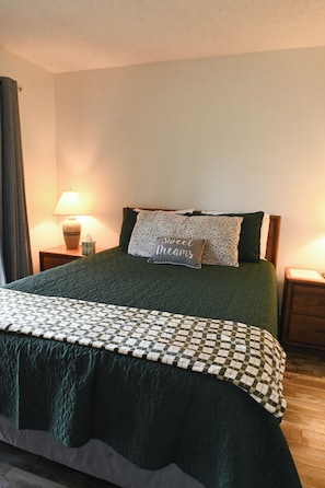 Ein ordentlich bezogenes Bett mit einer grünen Tagesdecke, einer karierten Decke und zwei Kissen, eines mit Leopardenmuster und auf dem anderen steht 'Sweet Dreams'.