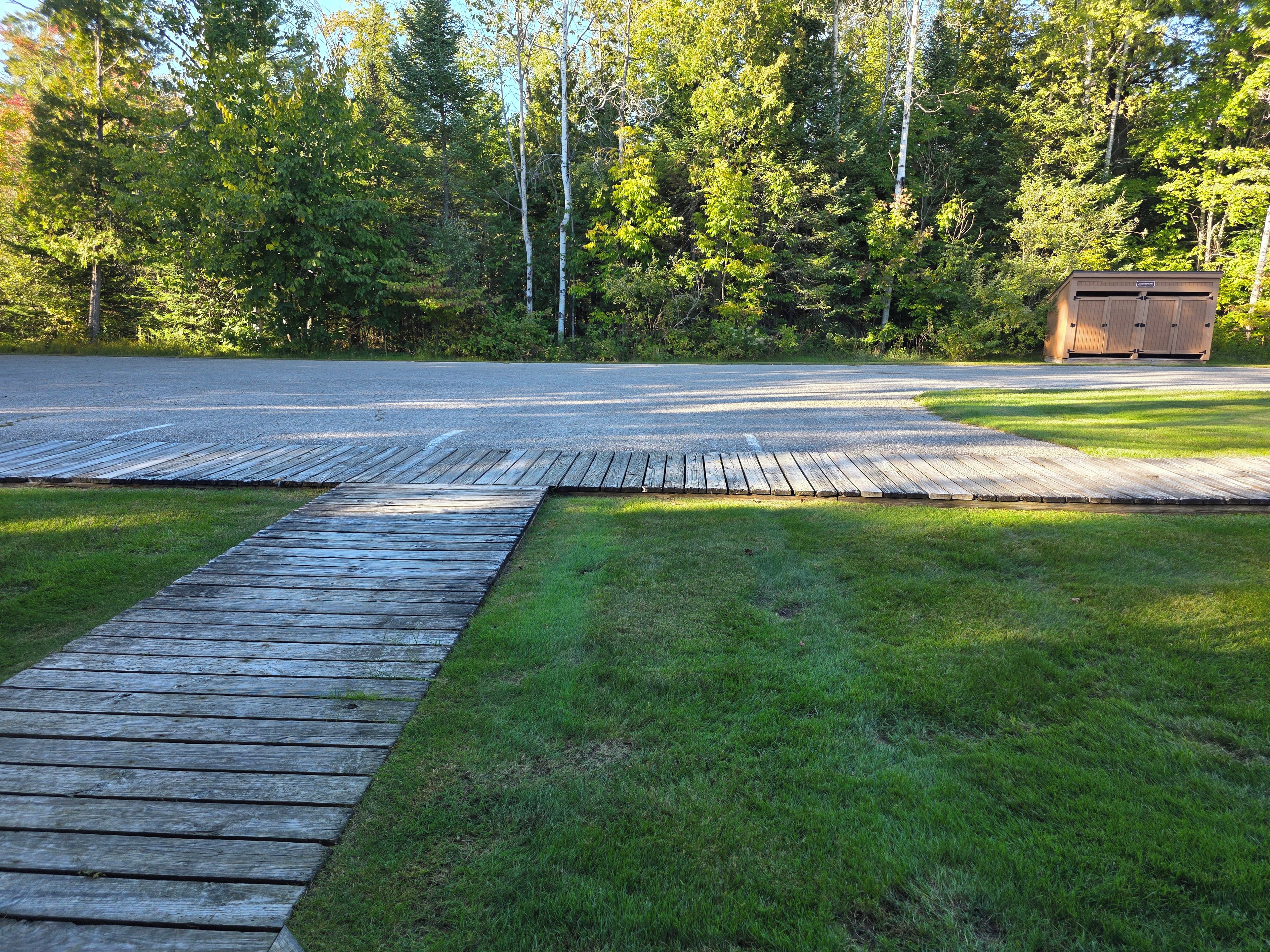 A wooden deck leading to a gravel driveway with a shed in the background.