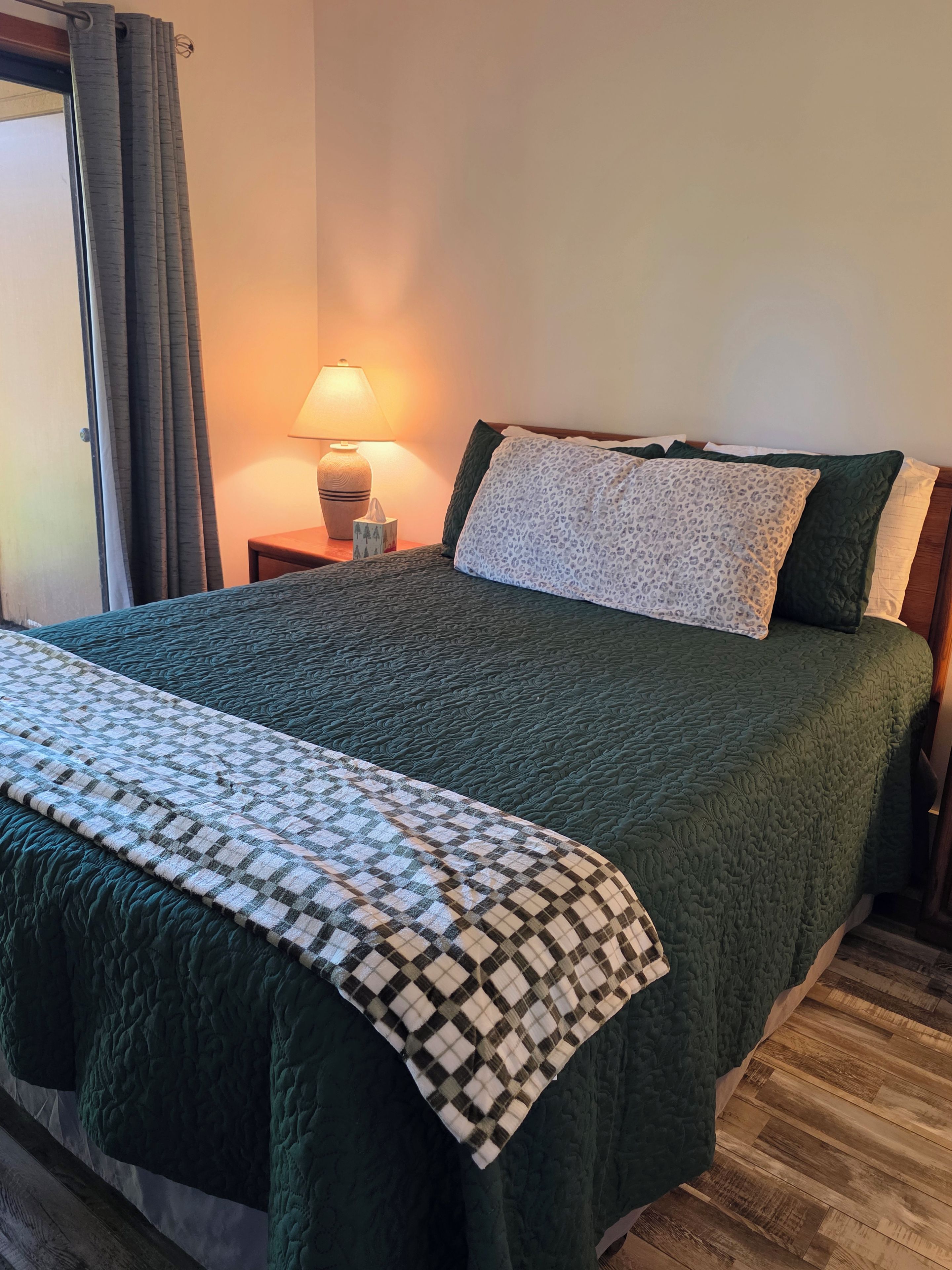 Un lit avec une couette verte, un plaid à carreaux et une table de chevet avec une lampe.