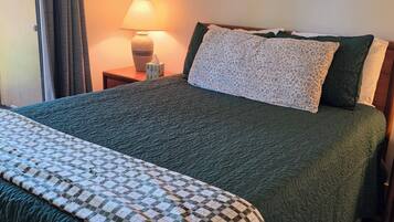 Un lit avec une couette verte, un plaid à carreaux et une table de chevet avec une lampe.