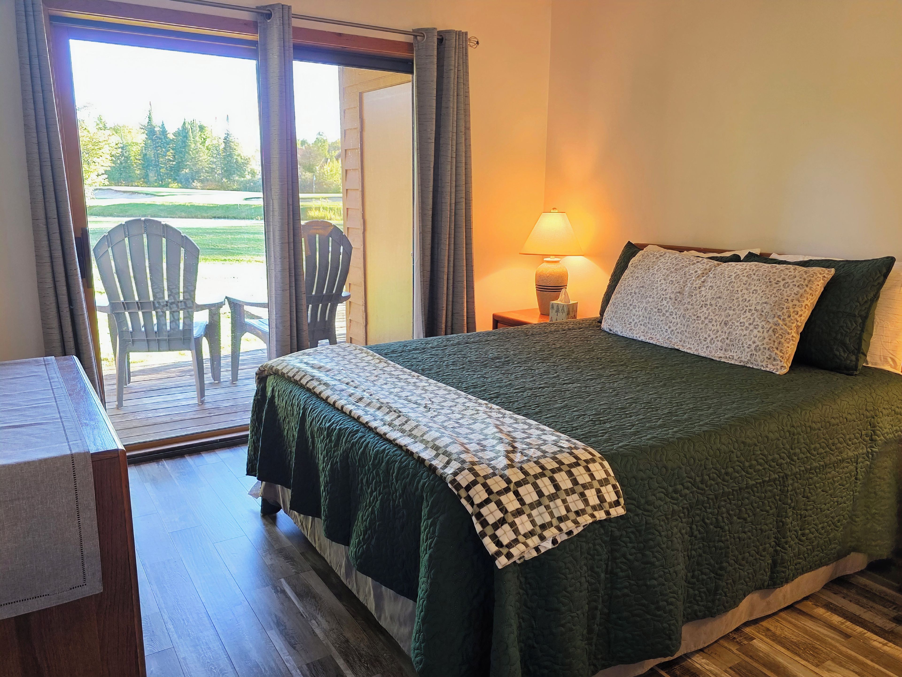 A bedroom with a bed, a nightstand, a lamp, and a view of the outdoors through a sliding door.