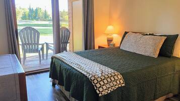 A bedroom with a bed, a nightstand, a lamp, and a view of the outdoors through a sliding door.