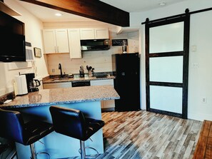 A kitchen with a bar area, a black refrigerator, and a wooden floor. - NEW rental Shanty Creek Resorts 1 bedroom on the Schuss course walk to slopes (Mancelona)