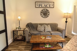 Un salon comprenant un canapé, une table basse, une horloge murale et une pancarte sur laquelle on peut lire : « Bienvenue chez nous ».