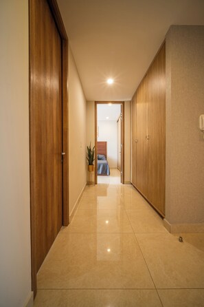 A hallway with wooden doors, a bed with a blue and white bedspread, and a potted plant. - Mazatlán Luxury Beach Residence - 606TN - Camino al Mar (Mazatlán)