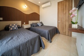 A hotel room with two beds, a wooden headboard, a nightstand, a bedside table, a wall-mounted air conditioner, a wooden wardrobe, and a potted orchid. - Mazatlán Luxury Beach Residence - 606TN - Camino al Mar (Mazatlán)