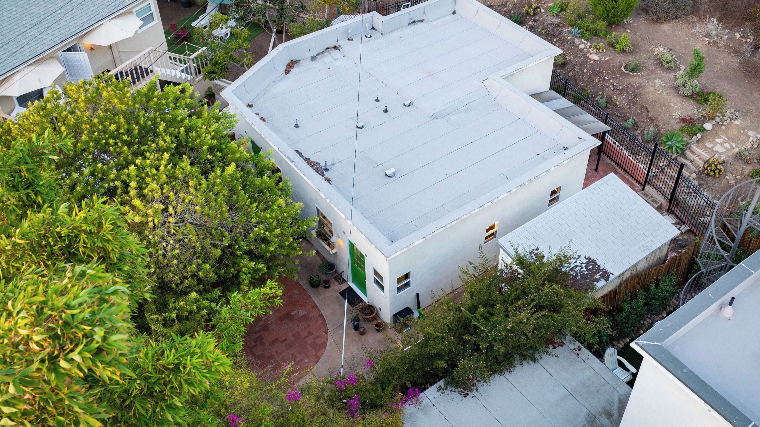A multi-story building with a flat roof, surrounded by greenery and a fenced yard.