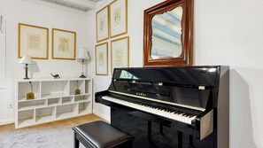 A piano room with a piano, a bench, a shelf with decorative items, and framed artwork on the wall. - Windansea Bungalow by Avantstay Beach Cottage + Garden Patio Walk to Beach + Mins to La Jolla (La Jolla)