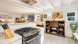 A kitchen with a gas stove, white cabinets, and a wooden cabinet with dishes. - Windansea Bungalow by Avantstay Beach Cottage + Garden Patio Walk to Beach + Mins to La Jolla (La Jolla)