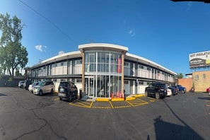 Un edificio con fachada curva, entrada de vidrio y estacionamiento con espacios reservados señalizados.