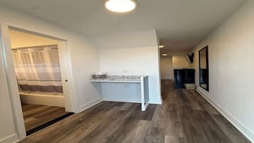 A hallway with a shower area, a small kitchenette, and a mirror on the wall.