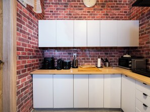 A compact kitchen with white cabinets, a brick wall, and a wooden countertop. - Łódź 1 Maja Central Room #1 (Łódź)