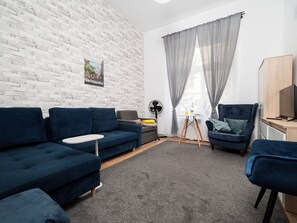 A modern living room with a white brick wall, a blue sofa, a grey armchair, a small table, and a TV on a wooden stand. - Łódź 1 Maja Central Room #1 (Łódź)