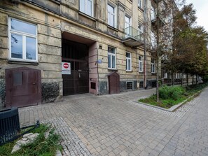 A building with a barred entrance, a no entry sign, and a street with trees and a trash bin. - Łódź 1 Maja Central Room #1 (Łódź)