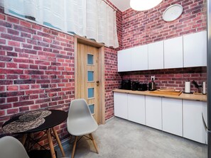 A compact kitchen with a brick wall, a wooden door, white cabinets, a coffee maker, and a small table with chairs. - Łódź 1 Maja Central Room #1 (Łódź)