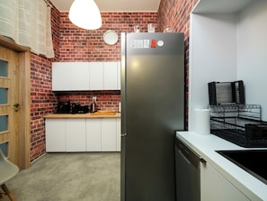 Eine kleine Küche mit Backsteinwand, einem Edelstahlkühlschrank, weißen Schränken, einer Holz Arbeitsplatte und einer Pendelleuchte.