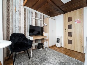 A room with a wooden ceiling, a television on a wooden stand, a black chair, a white desk, a white wardrobe, a white door with a window, and a white radiator. - Łódź 1 Maja Central Room #3 (Łódź)