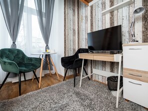 A room with a wooden desk, a flat-screen TV, two chairs, a small table with a cup and a plate, and a grey shaggy rug. - Łódź 1 Maja Central Room #3 (Łódź)