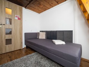 Quarto pequeno e moderno com sofá cinza, porta de madeira com painéis de vidro e carpete cinza.
