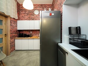A compact kitchen with a brick wall, a stainless steel refrigerator, white cabinets, a wooden countertop, and a hanging light fixture. - Łódź 1 Maja Central Room #3 (Łódź)