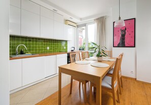 A modern kitchen with white cabinets, a green backsplash, and a dining area with a wooden table and chairs. - Nowolipki Cozy Soul Apartment (Warszawa)