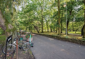 Een verhard pad in een park met bomen, een lantaarnpaal en een fietsenrek met een fiets.