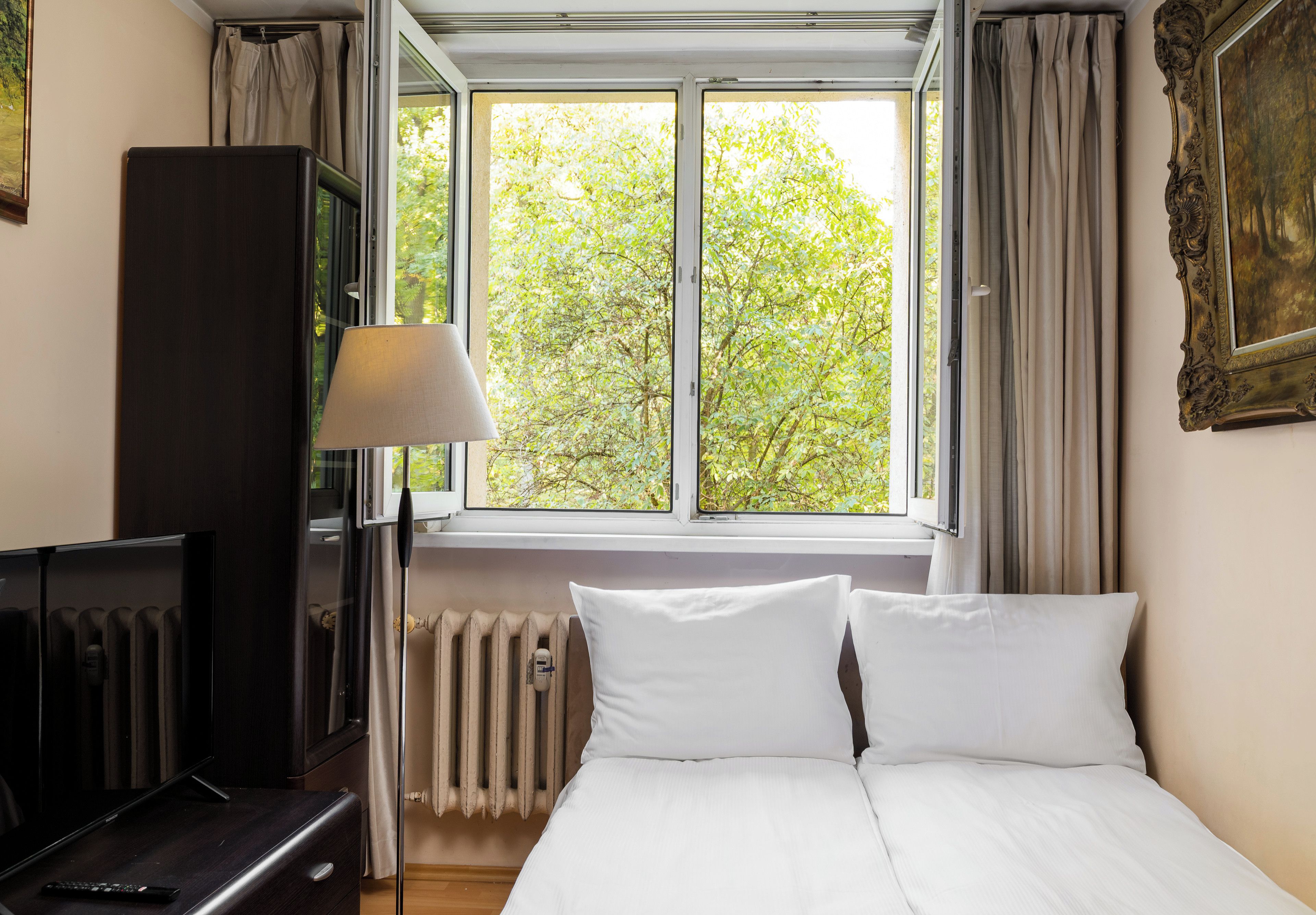 Een hotelkamer met een bed, een bureau, een lamp, een radiator en een raam met gordijnen.