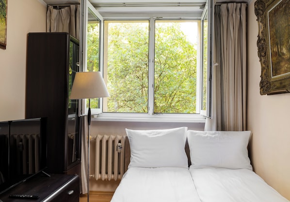 Een hotelkamer met een bed, een bureau, een lamp, een radiator en een raam met gordijnen.